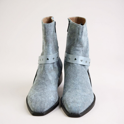 JO Ghost Pair of light blue suede boots with straps on a light gray 
